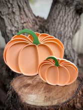 Load image into Gallery viewer, Two pumpkin-shaped cookie cutters on a wooden surface with a tree trunk background.